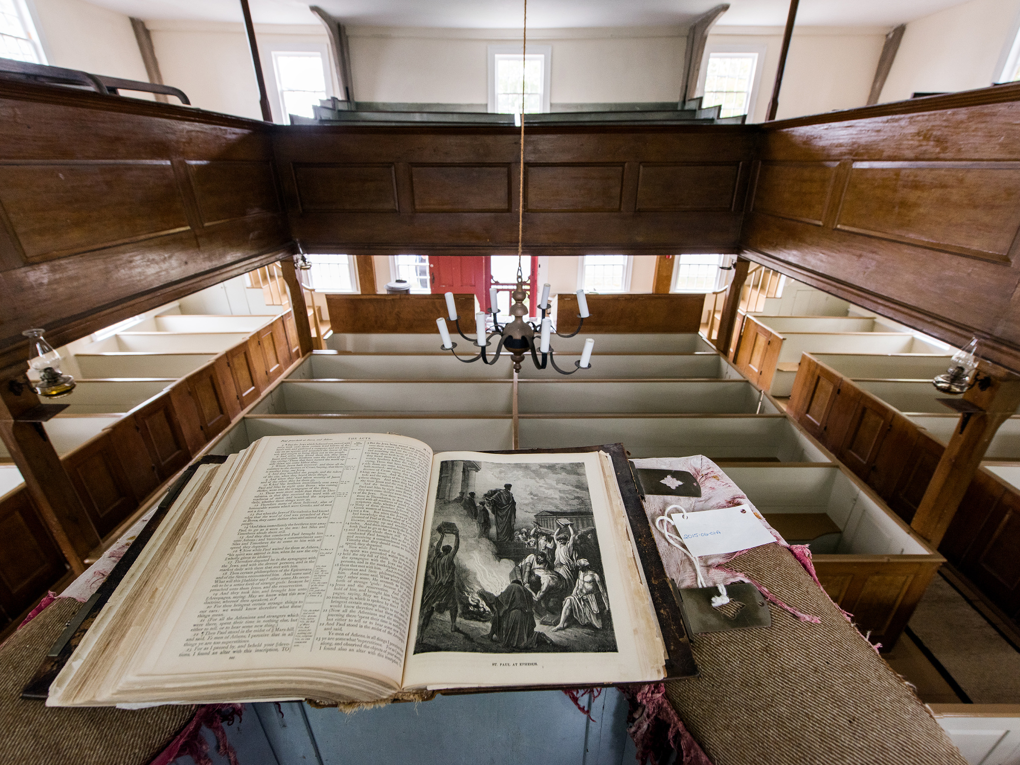 An interior view of a church from a high angle, showing rows of empty pews, a pulpit with an open book.